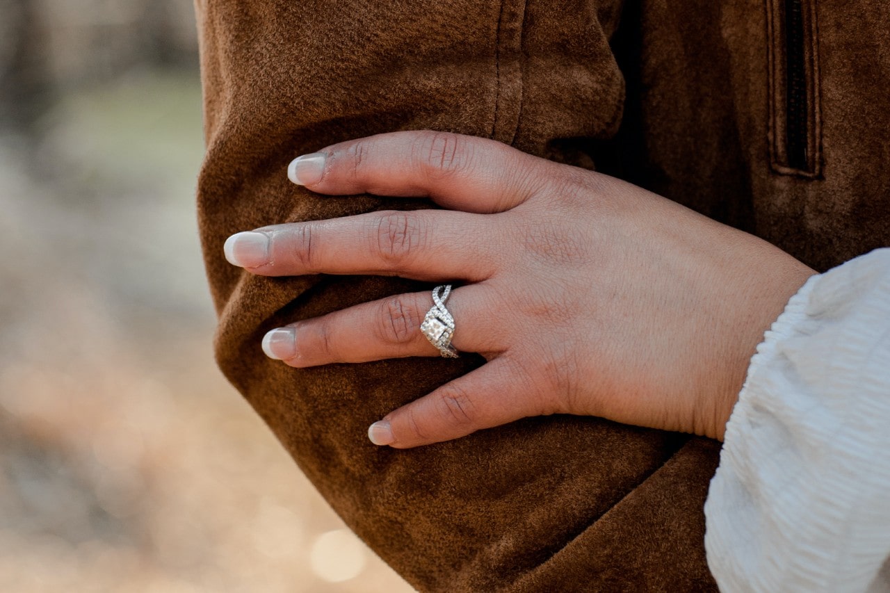 a woman’s hand resting on a man’s arm and wearing a princess cut engagement ring