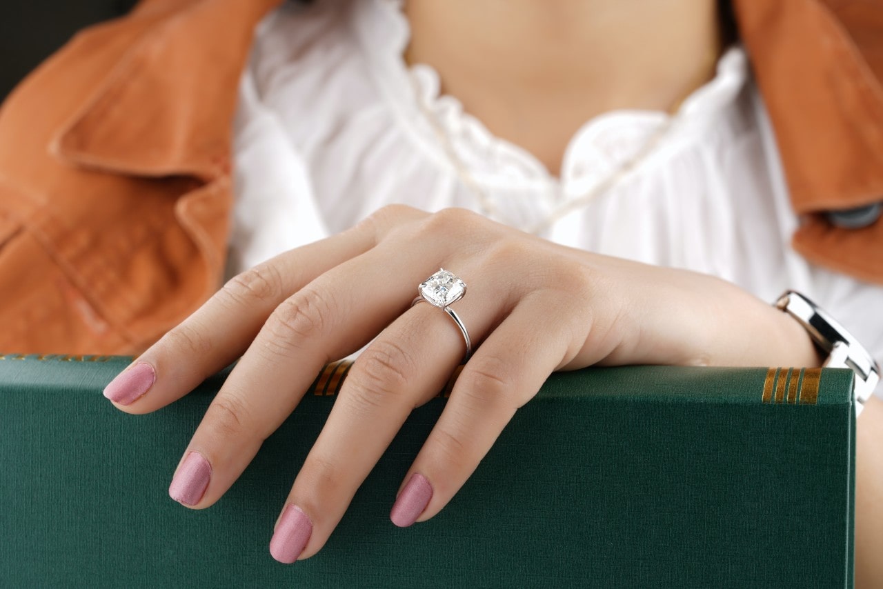 a woman’s hand resting on a green book and wearing a princess cut engagement ring