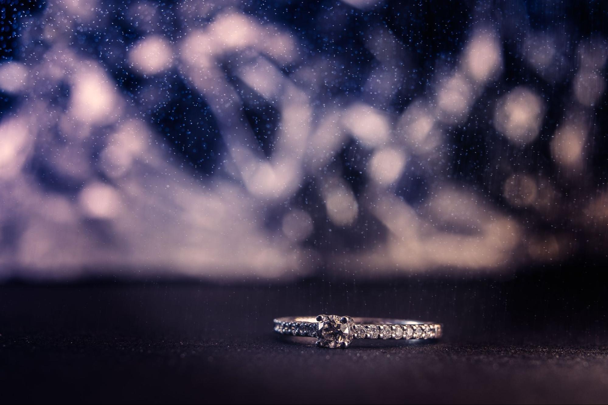 A white gold side stone engagement ring against a dark sparkly background.