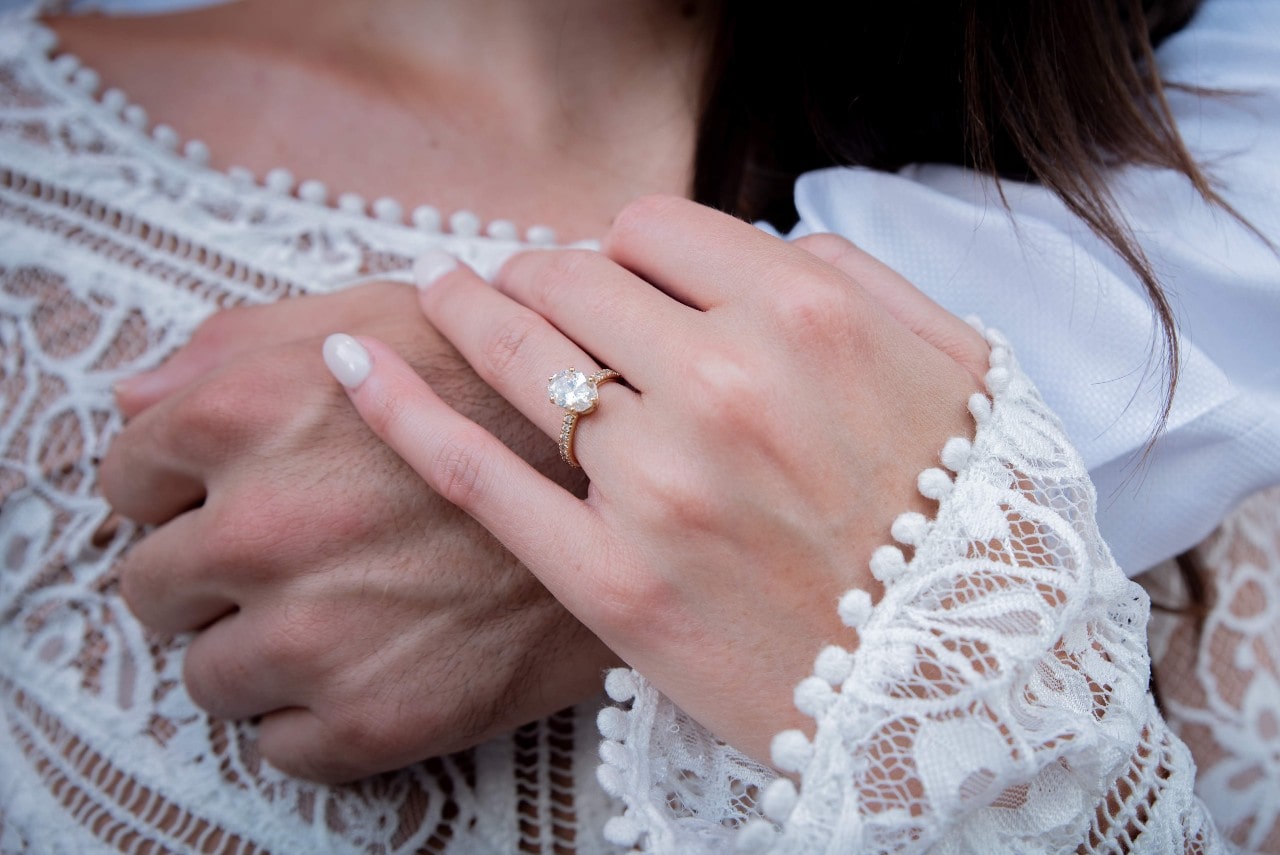 A bride with an oval-cut diamond side stone ring rests her hand on her groom’s.