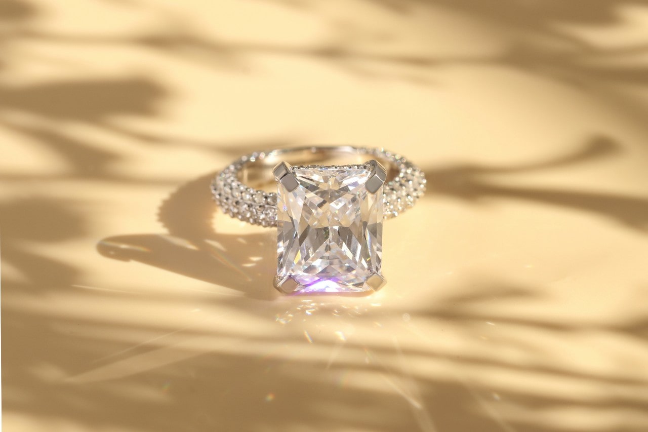 A diamond side stone engagement ring sitting outside on a tan surface.