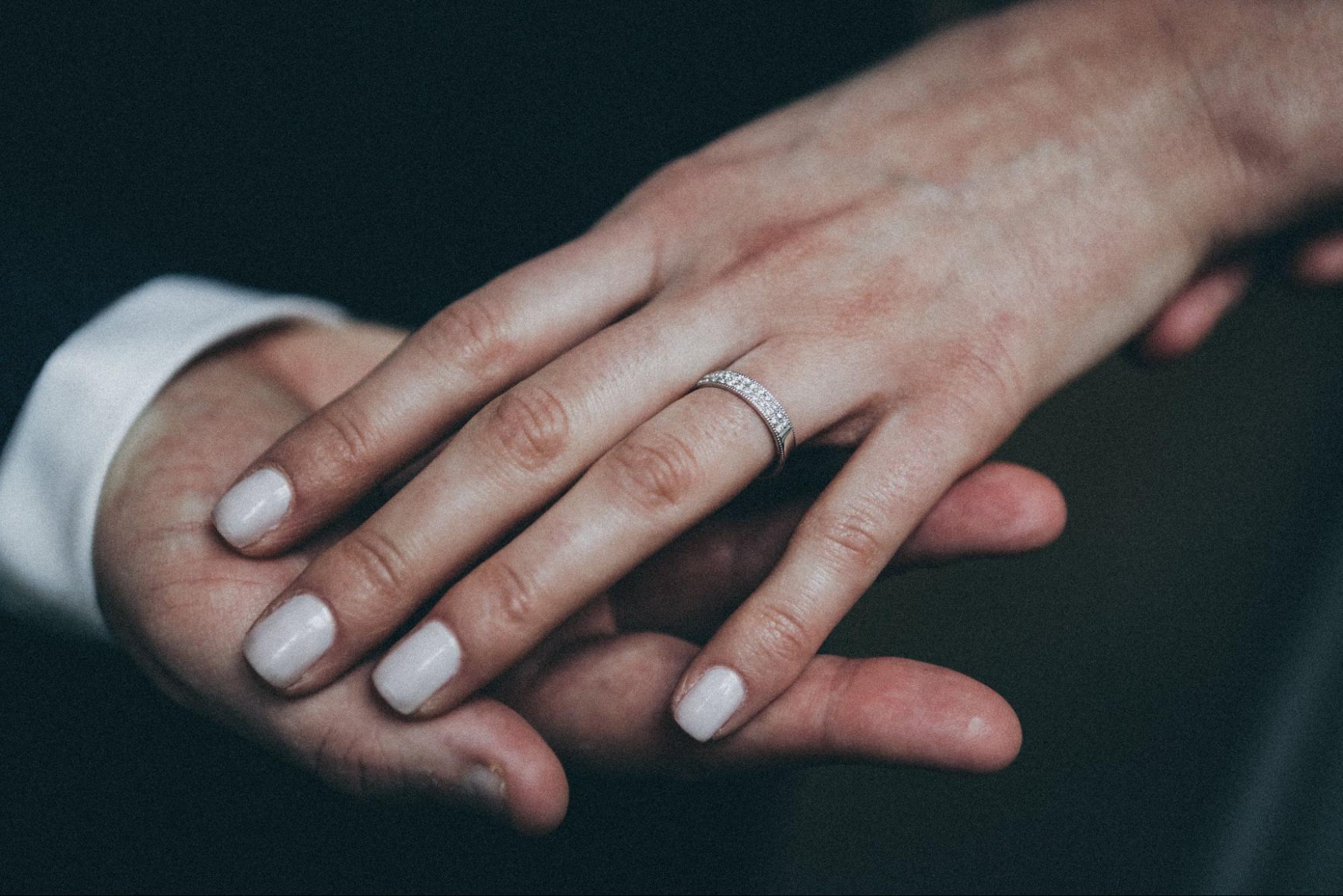 A woman’s hand with manicure showcasing a diamond wedding band on top of the man’s hand