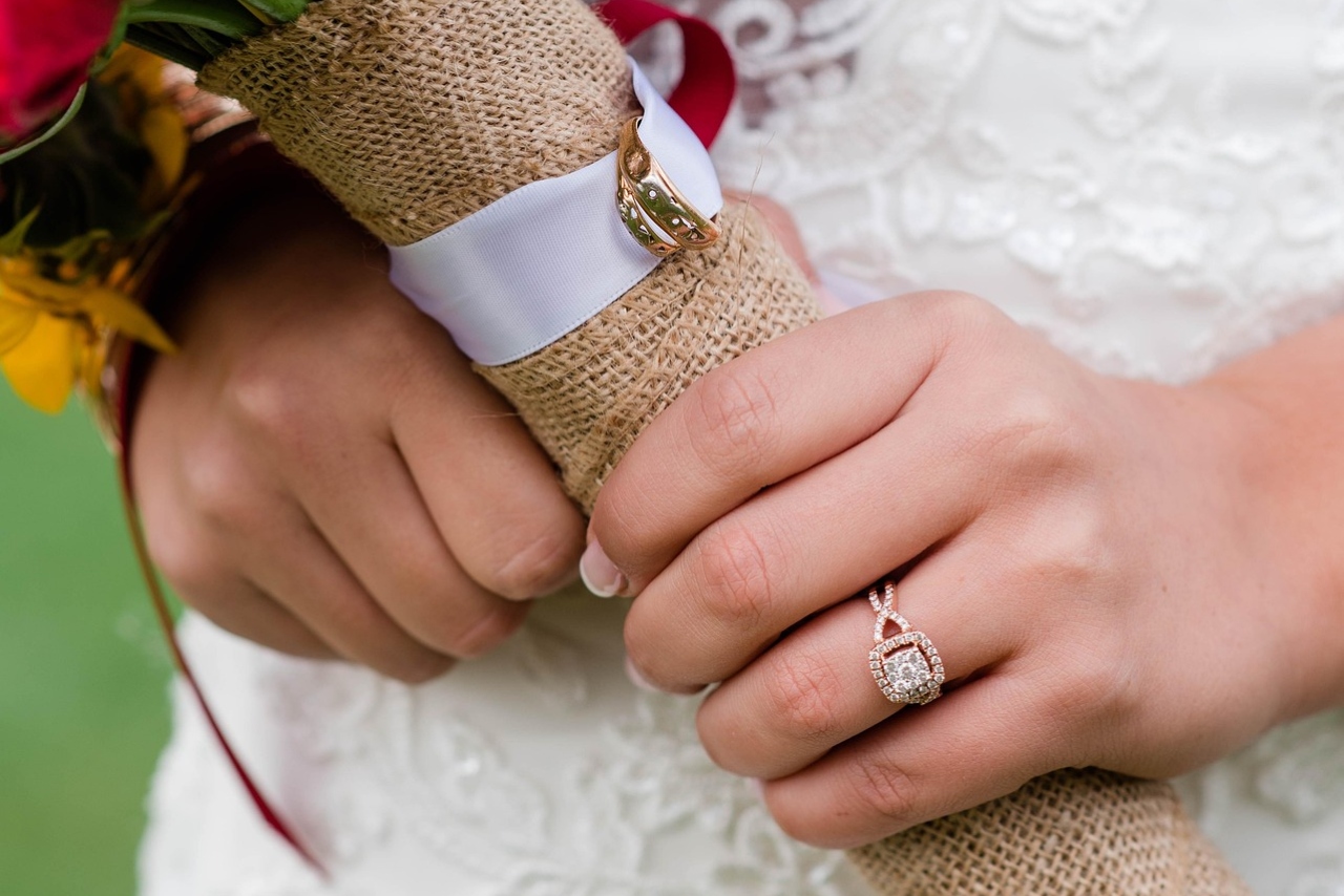 A close up of a bride in embroidered dress holding a bouquet, showcasing rose gold side stone diamond engagement ring.