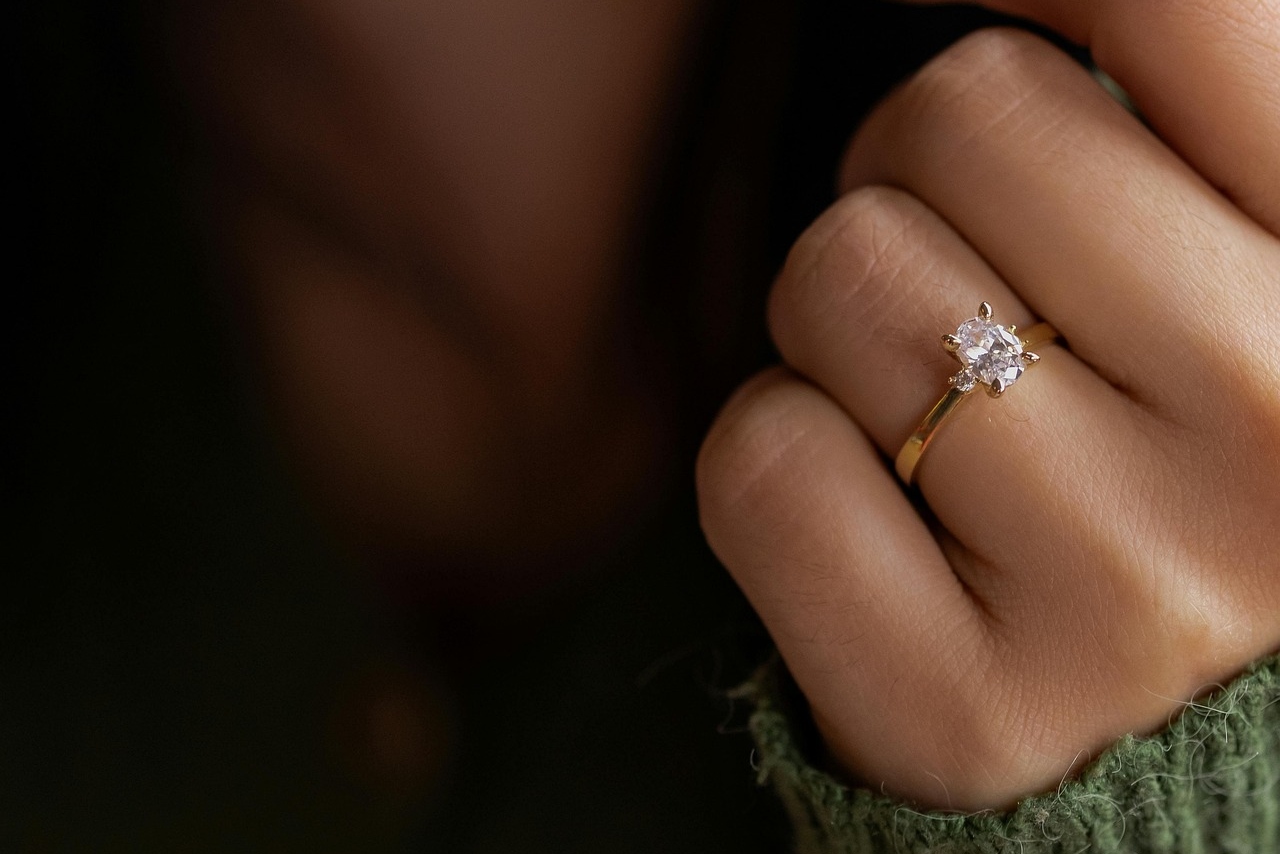 A close up of a yellow gold solitaire diamond engagement ring on a woman’s hand.
