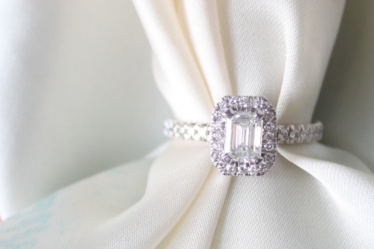 a silver halo engagement ring threaded onto a piece of white cloth a silver halo engagement ring threaded onto a piece of white cloth