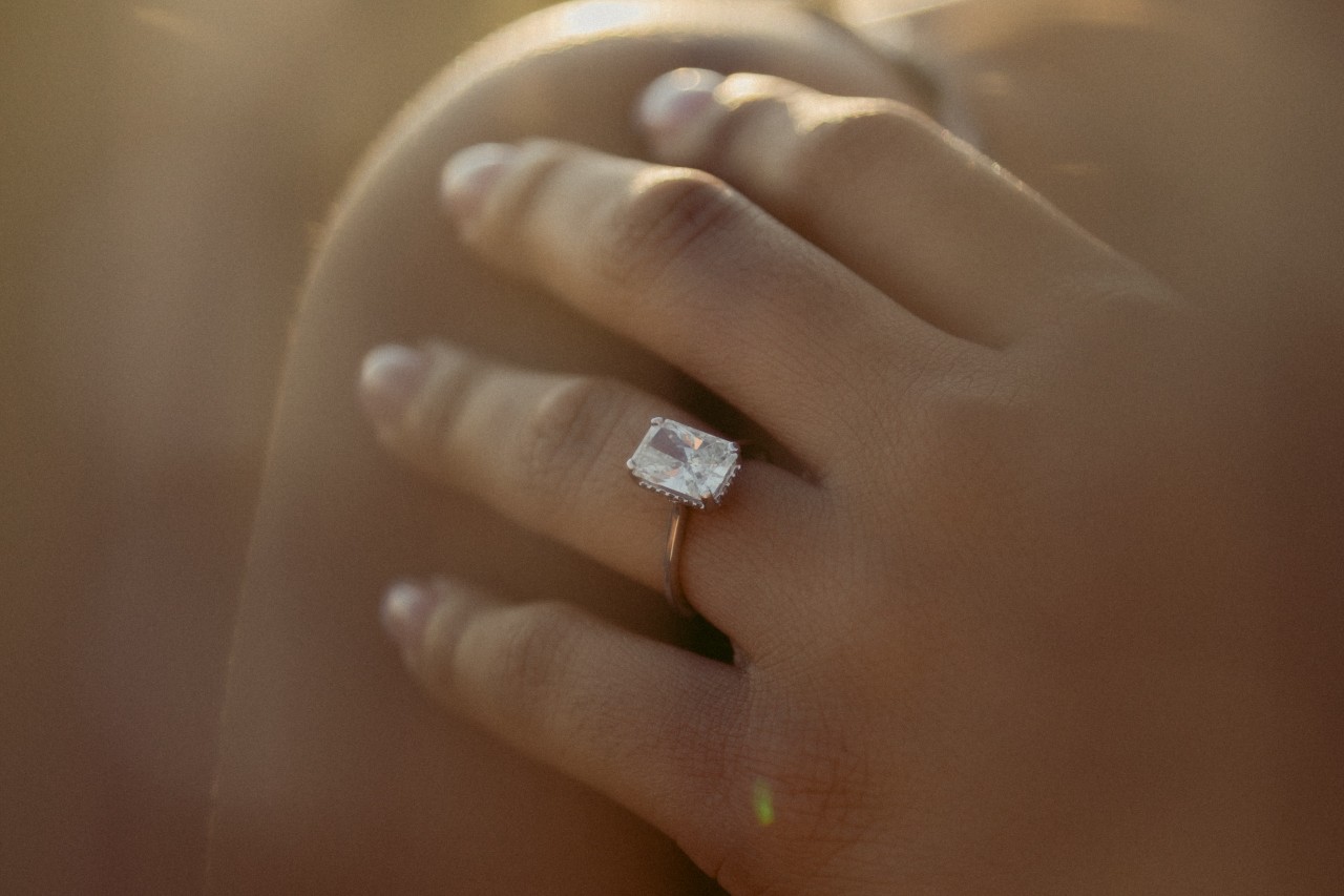 a woman’s hand resting on her shoulder wearing a gold solitaire engagement ring 