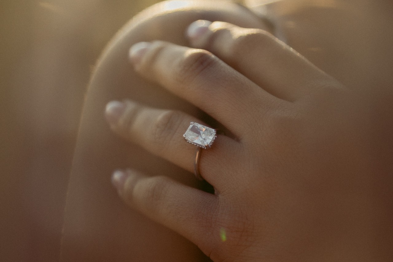 a woman’s hand resting on her shoulder wearing a gold solitaire engagement ring a woman’s hand resting on her shoulder wearing a gold solitaire engagement ring