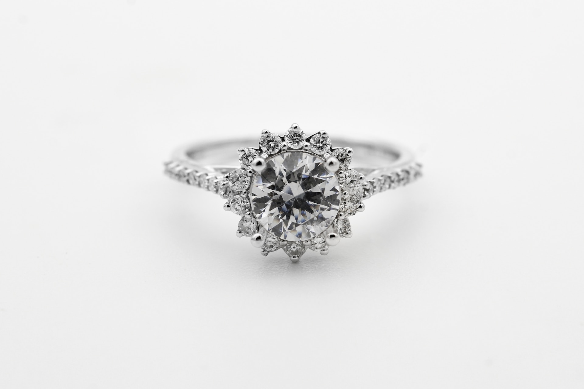 a white gold engagement ring with a floral halo and round cut center stone a white gold engagement ring with a floral halo and round cut center stone