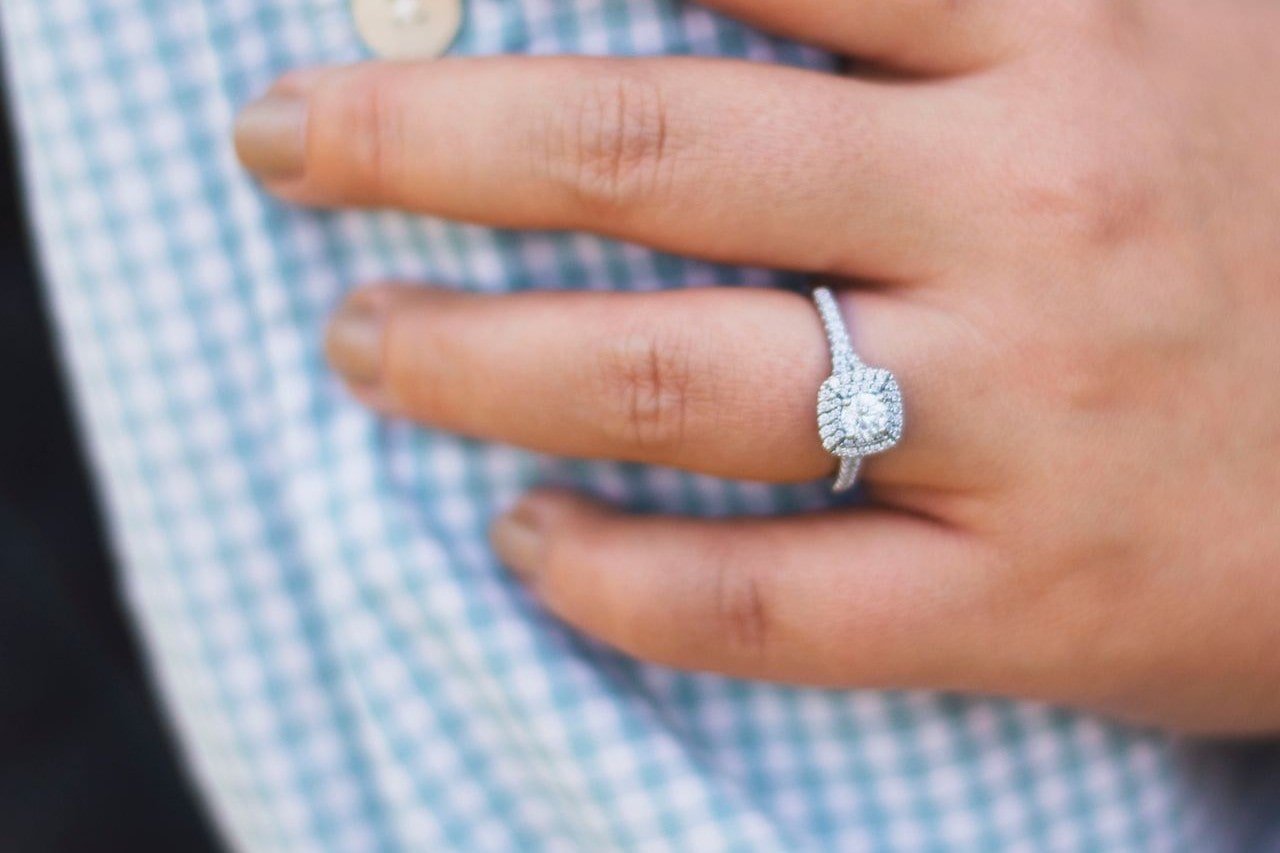 A woman rests her hand on her partner’s arm, wearing a halo ring.