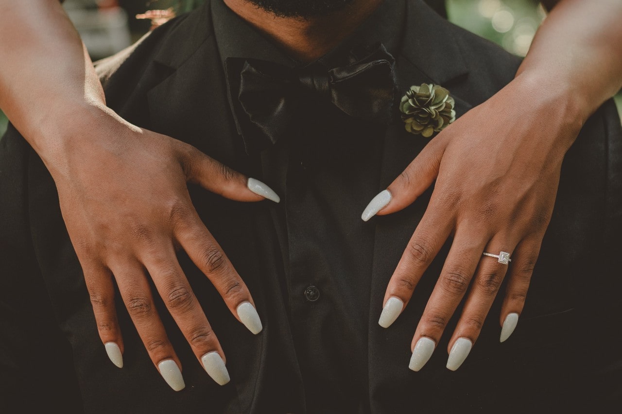 A couple embraces, the bride-to-be wearing a halo engagement ring.