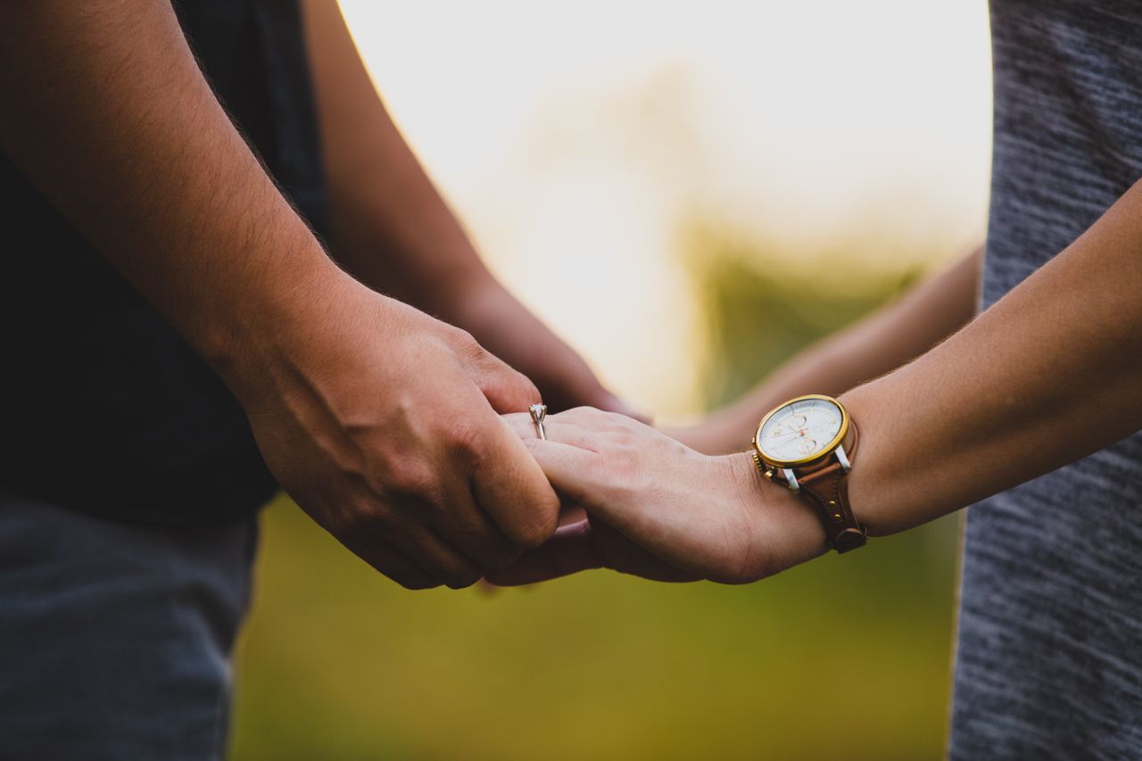 A couple holds hands, the woman wearing a solitaire engagement ring.