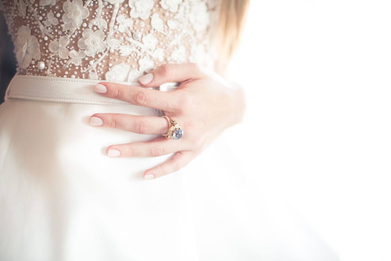A bride stands in front of a window before the wedding, wearing a blue topaz ring. A bride stands in front of a window before the wedding, wearing a blue topaz ring.