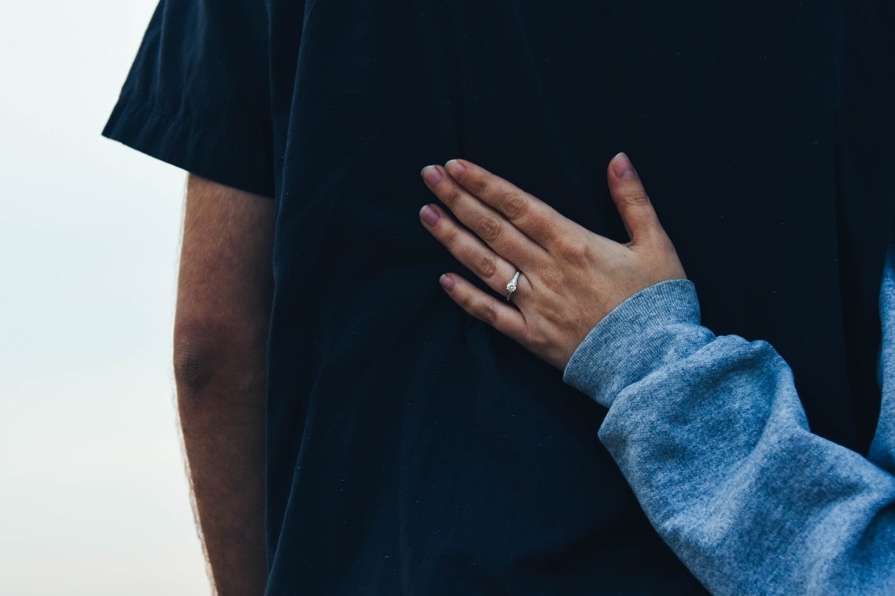 A woman rests her hand on her fiance’s chest, showing off her engagement ring.