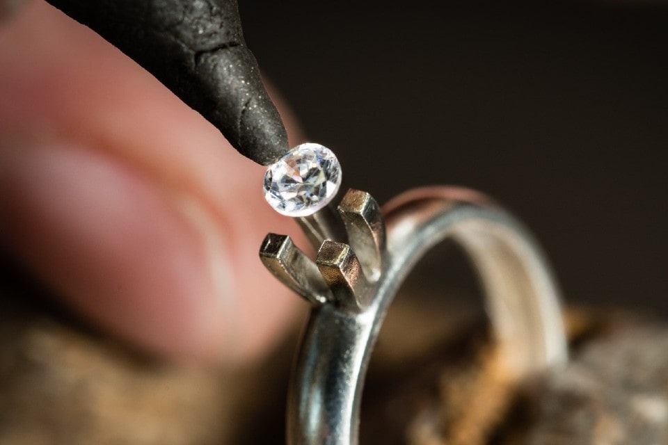 A jeweler carefully places a small lab-grown diamond into a solitaire ring setting.