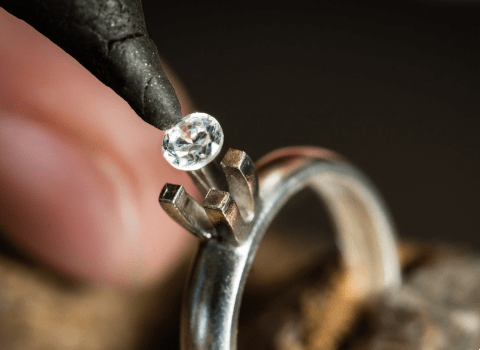 A jeweler carefully places a small lab-grown diamond into a solitaire ring setting.