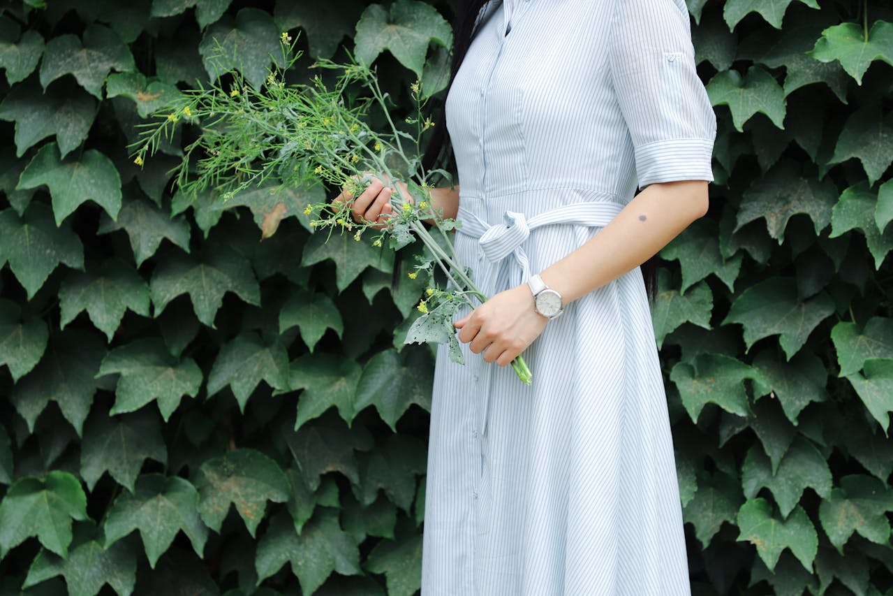 A woman in a blue dress holding flowers and wearing a white watch.